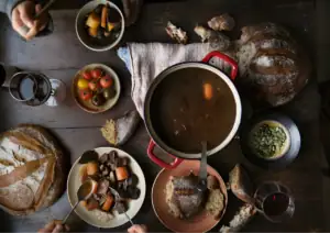 Cozy rustic meal with bread, stew, and fresh vegetables on a wooden table.